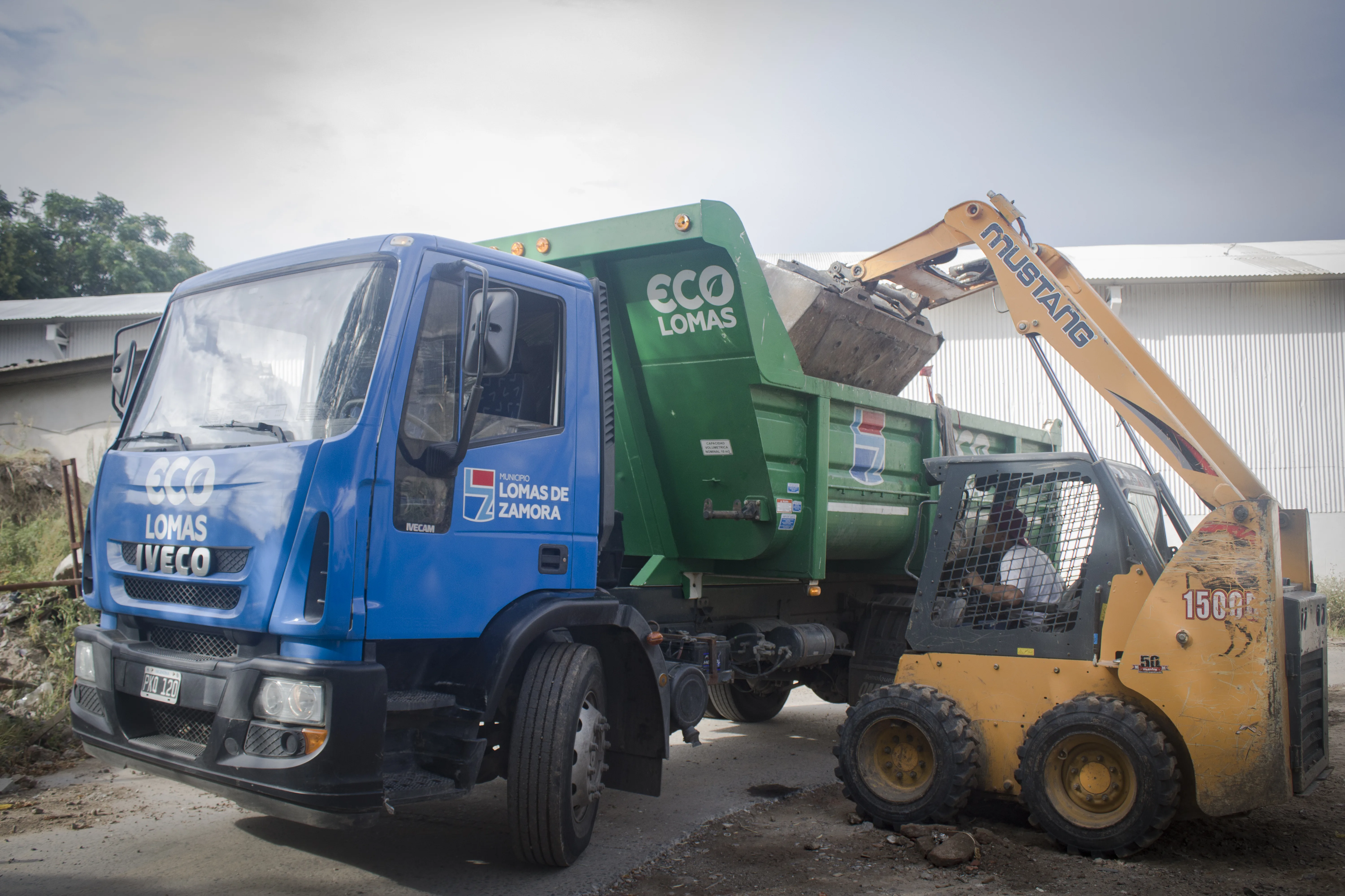 Camión de reciclado trabajando junto a una minicargadora
